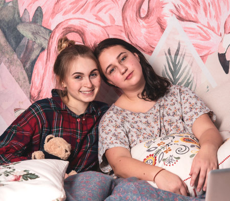 Two teenage girls on a dismantled bed in colorful pajamas.Girlfriends at home.の写真素材