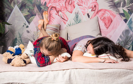 Two teenage girls on a dismantled bed in colorful pajamas.Girlfriends at home.の写真素材