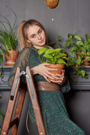 A blonde girl in a chiffon green dress with a flower pot in her hands on a wooden stepladder.の写真素材