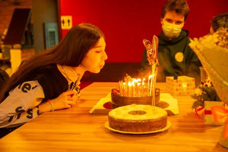 Russia, Moscow, December 2021. The celebration of the birthday. A teenage girl with dark hair blows out the candles on the cake.のeditorial素材
