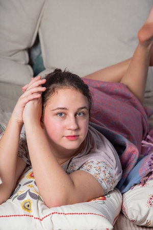 A teenage girl in pajamas is lying on the bed hugging a pillow.の写真素材