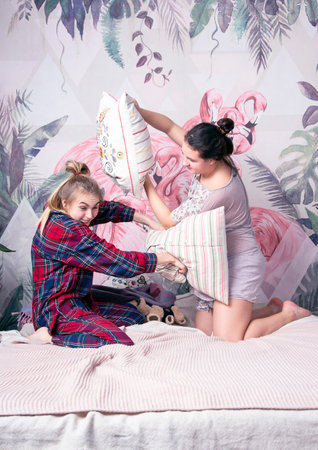 Two cute teenage girls in pajamas are fighting with pillows on the bed.の写真素材