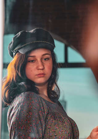 A charming teenage girl with dark hair in a black cap looks at herself in the mirror.の写真素材