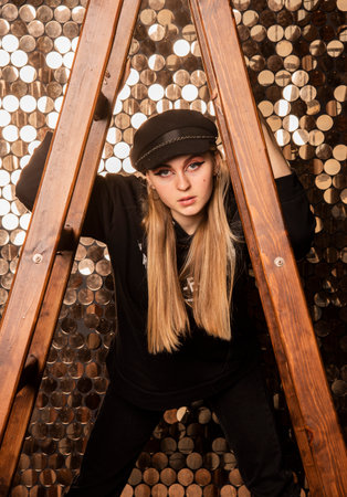 Women's photo shoot. A teenage girl in black clothes holds on to a stepladder against a golden wall.の写真素材