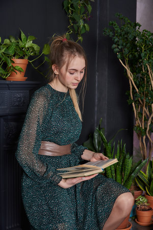 A blonde girl in a chiffon green dress with a book in hand in a cozy room.の写真素材
