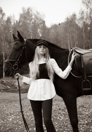 Black and white portrait of a young blonde girl holding the reins of a horse on a cloudy autumn day.の写真素材