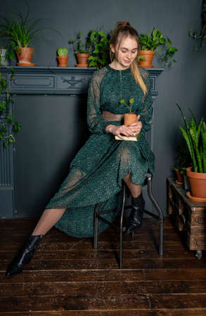 A blonde girl in a chiffon green dress with a book in hand in a cozy room.の写真素材