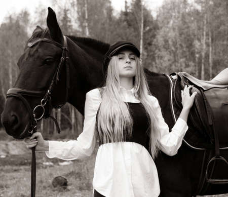 Black and white portrait of a young blonde girl holding the reins of a horse on a cloudy autumn day.の写真素材