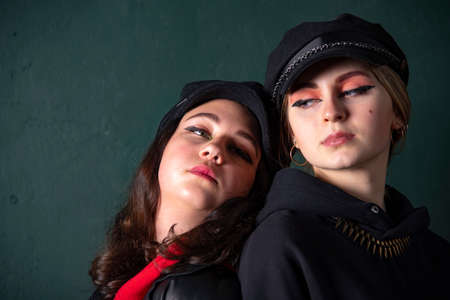 Two charming teenage girls with bright makeup, dressed in a grunge style, against a dark wall, a photo shoot in the studio. Youth trend.の写真素材