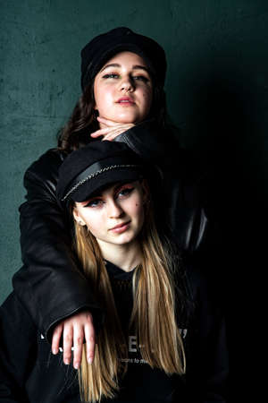 Two charming teenage girls with bright makeup, dressed in a grunge style, against a dark wall, a photo shoot in the studio. Youth trend.の写真素材