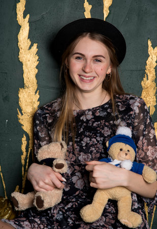A charming teenage girl in a black hat and with soft toys in her hands on the background of a gray wall.の写真素材