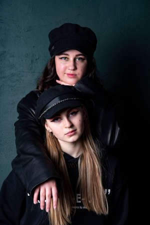 Two charming teenage girls with bright makeup, dressed in a grunge style, against a dark wall, a photo shoot in the studio. Youth trend.の写真素材