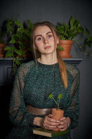 A blonde girl in a chiffon green dress with a flower pot in her hands on the background of a gray wall.の写真素材