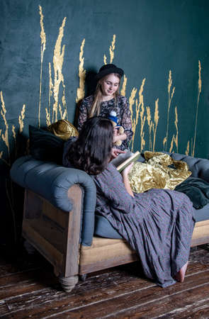 Two teen girl sitting on vintage sofa on the background of a gray wall with a pattern .の写真素材