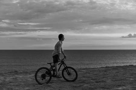 Crimea, Cape Tarkhankut, August 2020. Black and white photo of a young man with a bicycle on a beach.のeditorial素材
