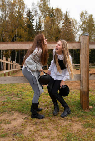 Two teenage girls in riding suits stand at a wooden fence on an autumn day.の写真素材