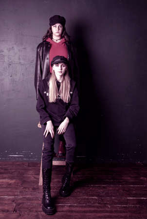 Two charming teenage girls with bright makeup, dressed in a grunge style, against a dark wall, a photo shoot in the studio. Youth trend.の写真素材