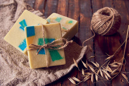 A fragrant organic handmade soap with a geometric pattern, a linen napkin and a few dry spikelets on a brown wooden countertop.の写真素材