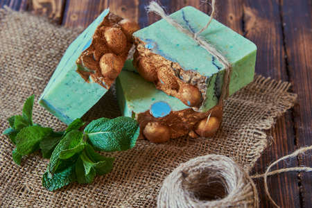 A fragrant green organic handmade soap decorated with mint leaves, burlap and coarse threads on a brown wooden countertop.の写真素材