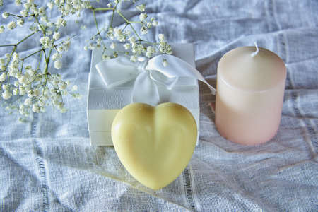 A fragrant organic handmade soap in the shape of a heart, a candle and flowers on a white linen fabric.の写真素材