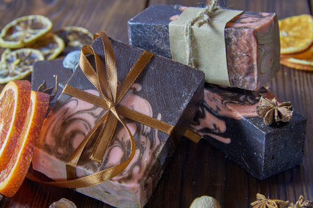 Scented organic dark handmade soap, scented spices and orange slices on a brown wooden countertop.の写真素材