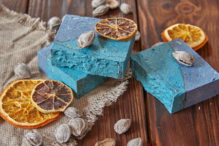 A fragrant, bright blue organic handmade soap, a linen napkin, and scented spices on a brown wooden countertop.の写真素材