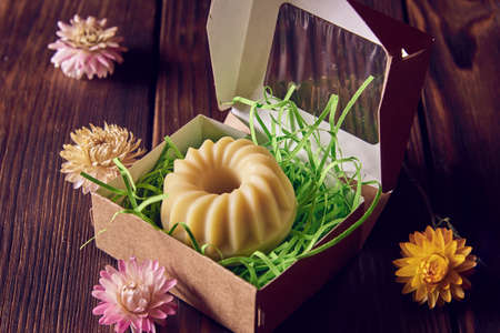 Fragrant organic handmade soap of unusual shape in a cardboard gift box and dried flowers on a dark wooden countertop.の写真素材