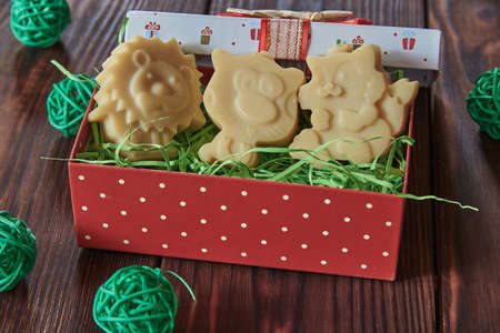 Handmade organic baby soap in the shape of animals in a bright red gift box and with different decor on a dark wooden table.の写真素材
