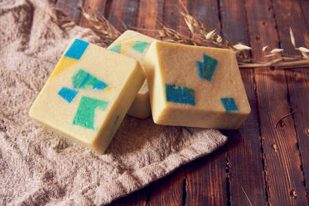 A fragrant organic handmade soap with a geometric pattern, a linen napkin and a few dry spikelets on a brown wooden countertop.の写真素材