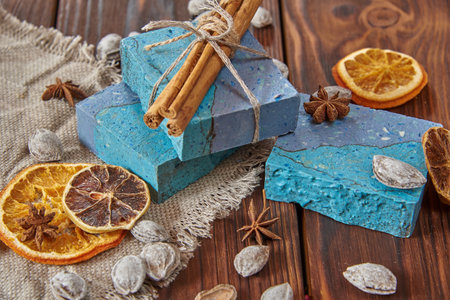 A fragrant, bright blue organic handmade soap, a linen napkin, and scented spices on a brown wooden countertop.の写真素材