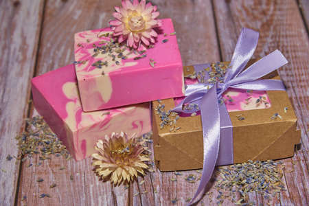 Fragrant pink organic handmade soap, gift box decorated with silk ribbon and dried flowers on the wooden countertop. Healthy lifestyle, eco-friendly products.の写真素材