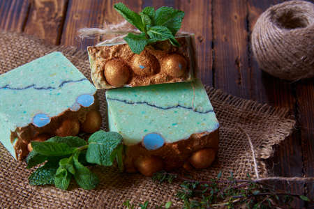 A fragrant green organic handmade soap decorated with mint leaves and burlap on a brown wooden countertop.の写真素材