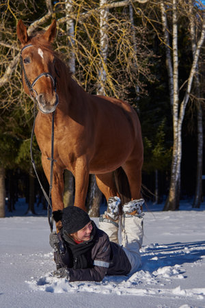 Russia, Moscow region, March 2021.A teenage girl lies on the white snow next to a graceful horse on a sunny winter day.のeditorial素材