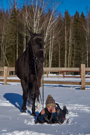 Russia, Moscow region, March 2021.A teenage girl lies on the white snow next to a graceful horse on a sunny winter day.のeditorial素材