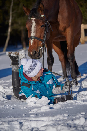 Russia, Moscow region, March 2021.A teenage girl lies on the white snow next to a graceful horse on a sunny winter day.のeditorial素材