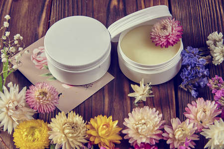 Handmade cream on a dark wooden surface surrounded by bright dried flowers. Healthy lifestyle, natural supplements.の写真素材