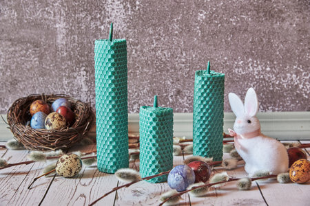 Three handmade wax candles and Easter decor on a gray wall background.の写真素材