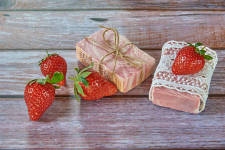 Pink textured handmade soap, vintage lace and delicious strawberries on a wooden background.の写真素材