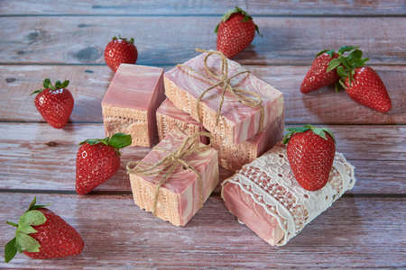Pink textured handmade soap, vintage lace and delicious strawberries on a wooden background.の写真素材