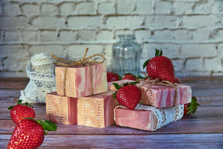Pink textured handmade soap, vintage lace and delicious strawberries on a wooden background.の写真素材