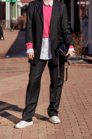 A woman in a black men's suit and white shirt, with fashion accessories, on a sunny spring day.の写真素材