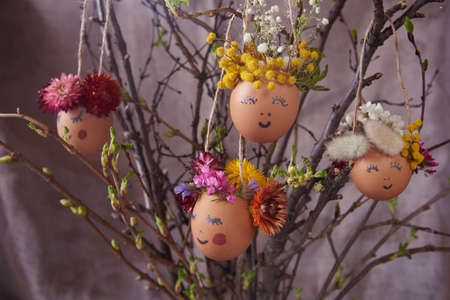 Natural easter eggs with funny painted face, decorated with bright flowers, hang on the branches.の写真素材