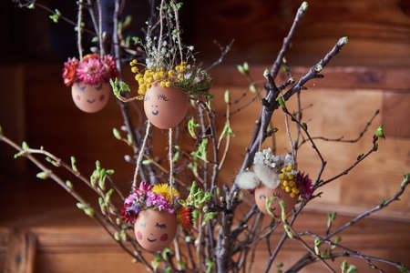 Natural easter eggs with funny painted face, decorated with bright flowers, hang on the branches.の写真素材