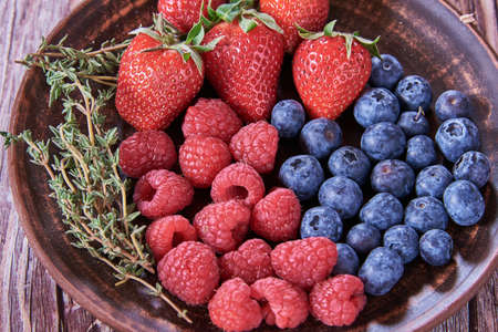 Ripe delicious berries on a ceramic plate on a wooden background.