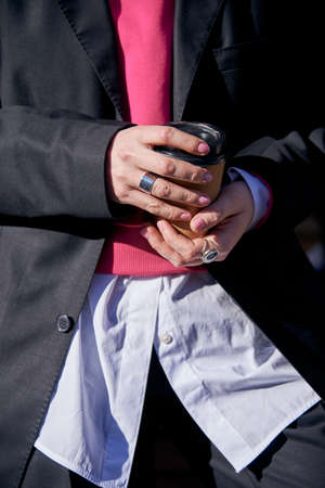 A woman in a black mens suit and white shirt with a disposable cup of coffee in her hands on a sunny day.の写真素材