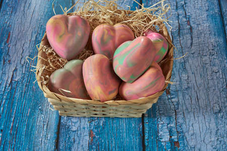 Fragrant multicolored organic handmade soap in the shape of a heart in a wicker basket on a blue...