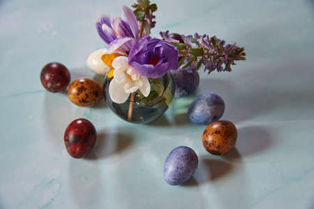 A small vase with spring flowers and painted quail Easter eggs on a light background.