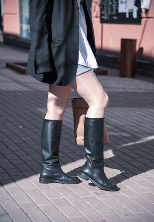 A woman in black leather boots, a black man's jacket, and a brown bag.の写真素材