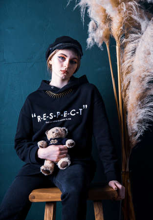 Russia, Moscow, February 2021. A teenage girl in a black hoodie and with a soft toy bear poses against a green wall in a photo studio.のeditorial素材