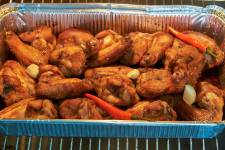 Chicken wings in marinade are baked in an aluminum form in the oven.の写真素材